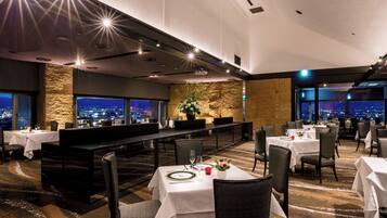 A modern dining area with tables set for meals, a long counter, and a city view through large windows.