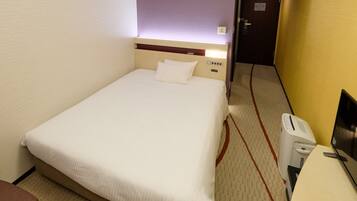 A hotel room with a single bed, a bedside table, a chair, and a desk with a computer.