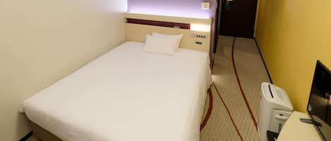 Habitación de hotel con una cama individual, una mesita de noche, una silla y un escritorio con una computadora.