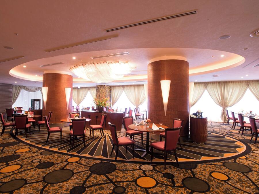 A hotel dining area with round tables, red chairs, and a patterned carpet.