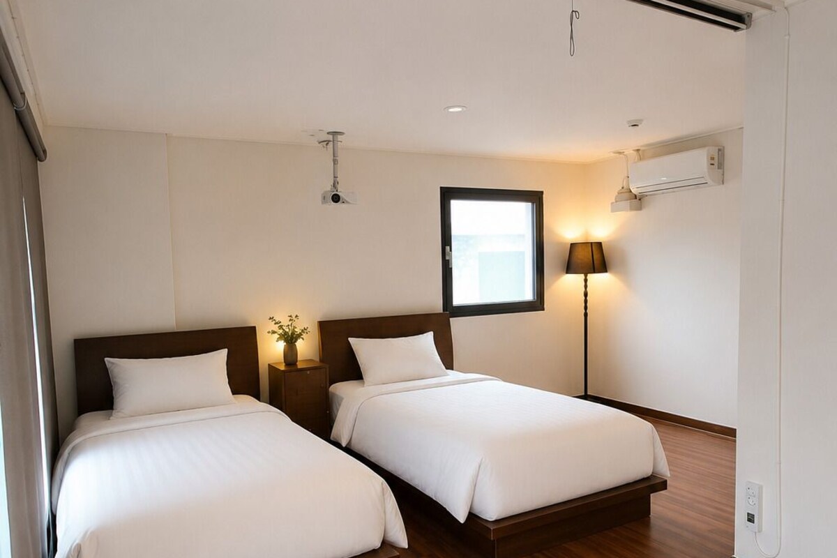 A hotel room with two beds, a window, an air conditioning unit, and a lamp.