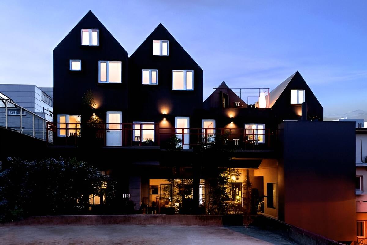 A modern multi-story building with multiple windows and balconies, featuring a mix of dark and light architectural elements.
