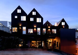 Un immeuble moderne à plusieurs étages, doté de nombreuses fenêtres et de balcons, et caractérisé par un mélange d’éléments architecturaux aux couleurs sombres et claires.
