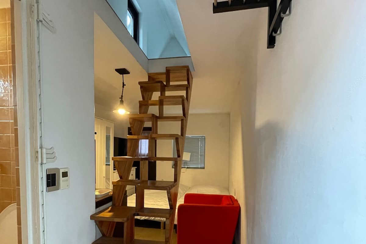 A modern interior with a wooden staircase, a red chair, and a ceiling light.