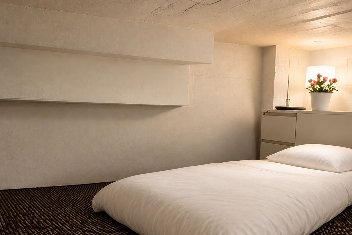 A hotel room with a bed, a wall-mounted shelf with a lamp, and a patterned carpet.