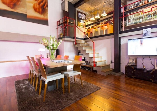 A modern dining area with a wooden table and chairs, a staircase with red railings, and a bar area with shelves of bottles. - iHouse ChinChin (Seoul)