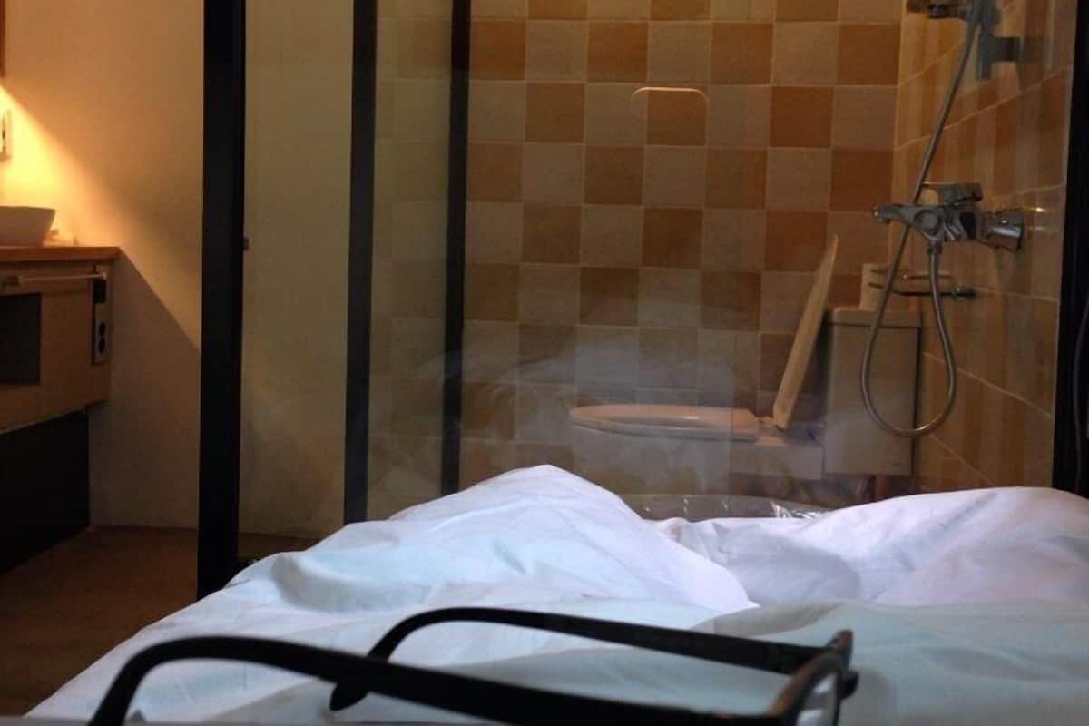A hotel room with a bed, a glass shower enclosure, and a checkered tile wall.