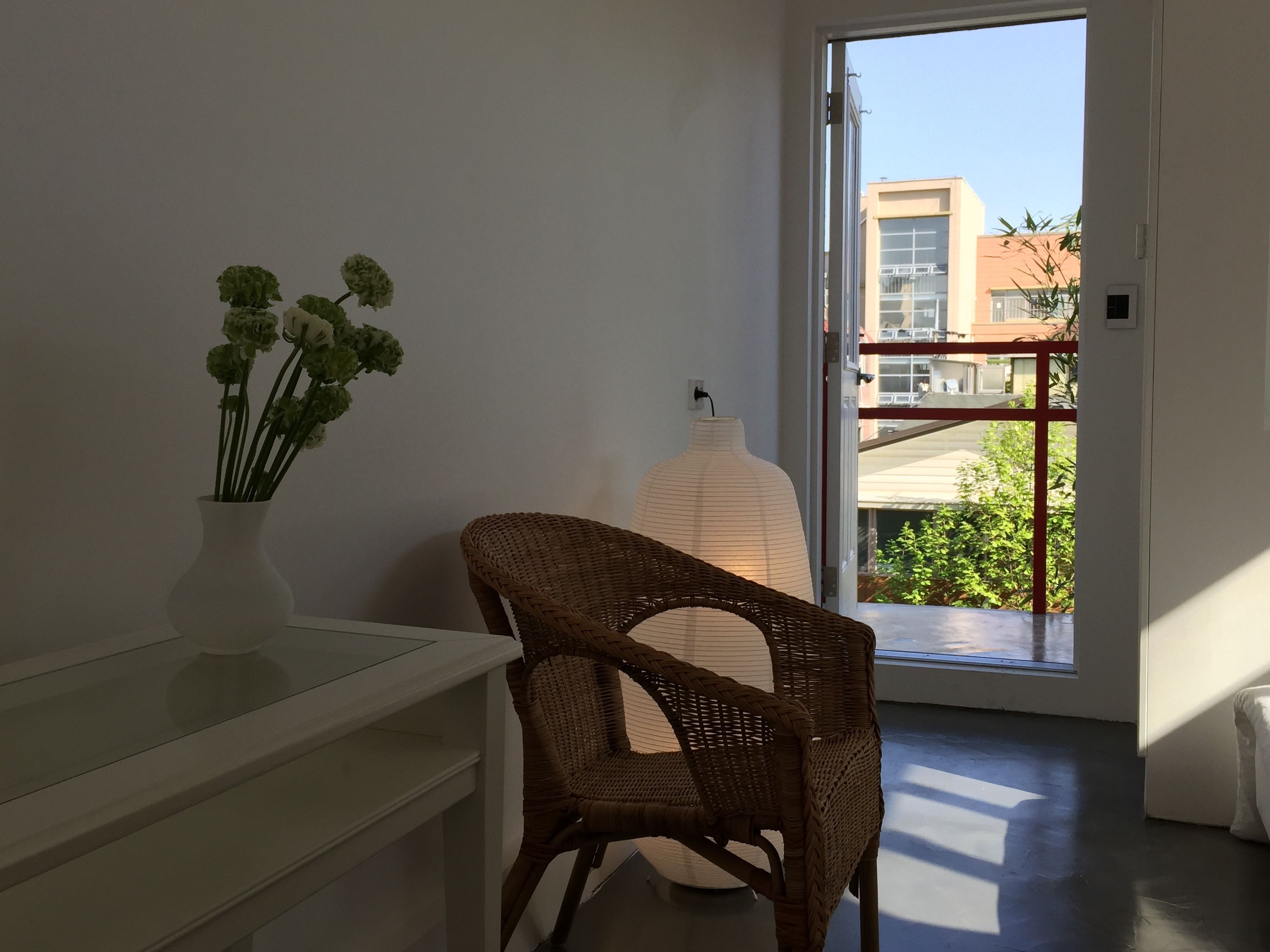 Une pièce comprenant un fauteuil en osier, un vase blanc orné de fleurs et une grande sculpture blanche.
