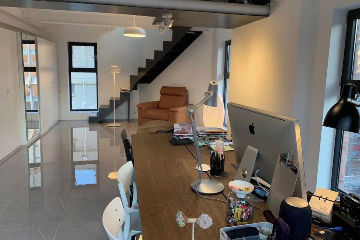 A modern living room with a wooden floor, a staircase, a sofa, and a desk with a computer.