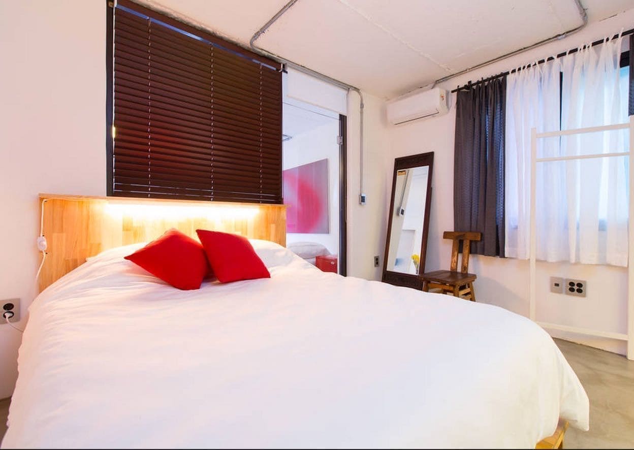 A bedroom with a large bed, a wooden headboard, a nightstand, a mirror, and a window with curtains.
