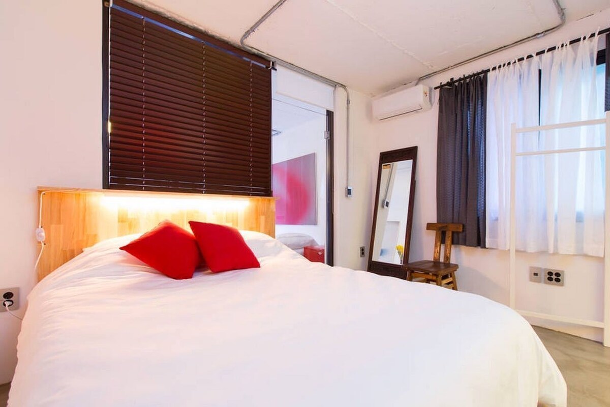 A bedroom with a large bed, a wooden headboard, a nightstand, a mirror, and a window with curtains.