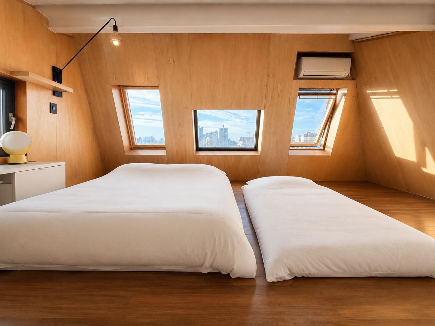 Una habitación moderna con dos camas, tragaluces, un escritorio y una lámpara.