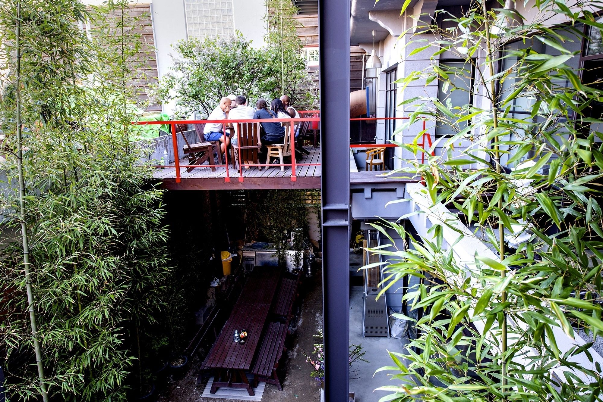 An outdoor seating area with bamboo plants, a wooden table, and a red railing.