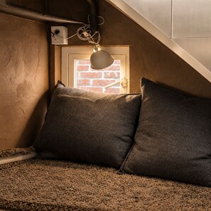 A cozy corner with a carpet, two pillows, a wall-mounted lamp, and a door with a brick pattern. - iHouse ChinChin (Seoul)