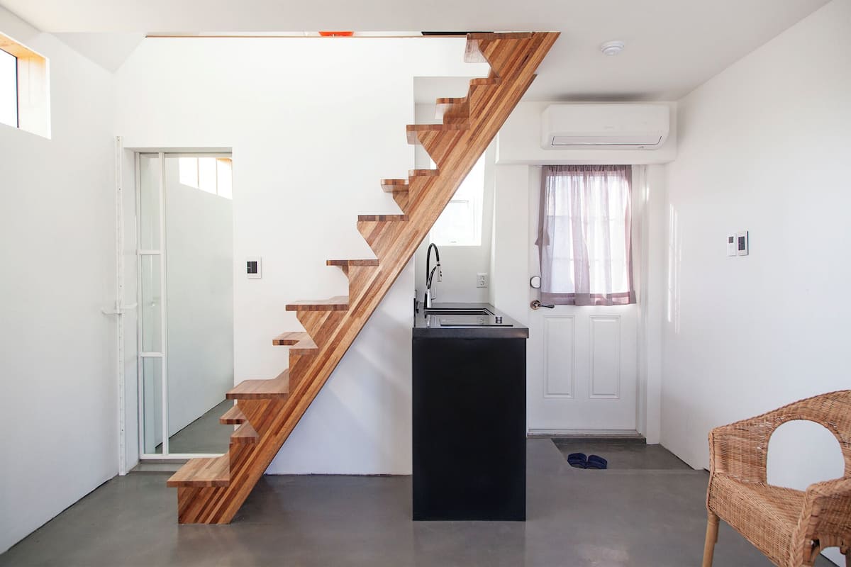 A modern interior with a wooden staircase, a black kitchen island, a white door, and a wicker chair.