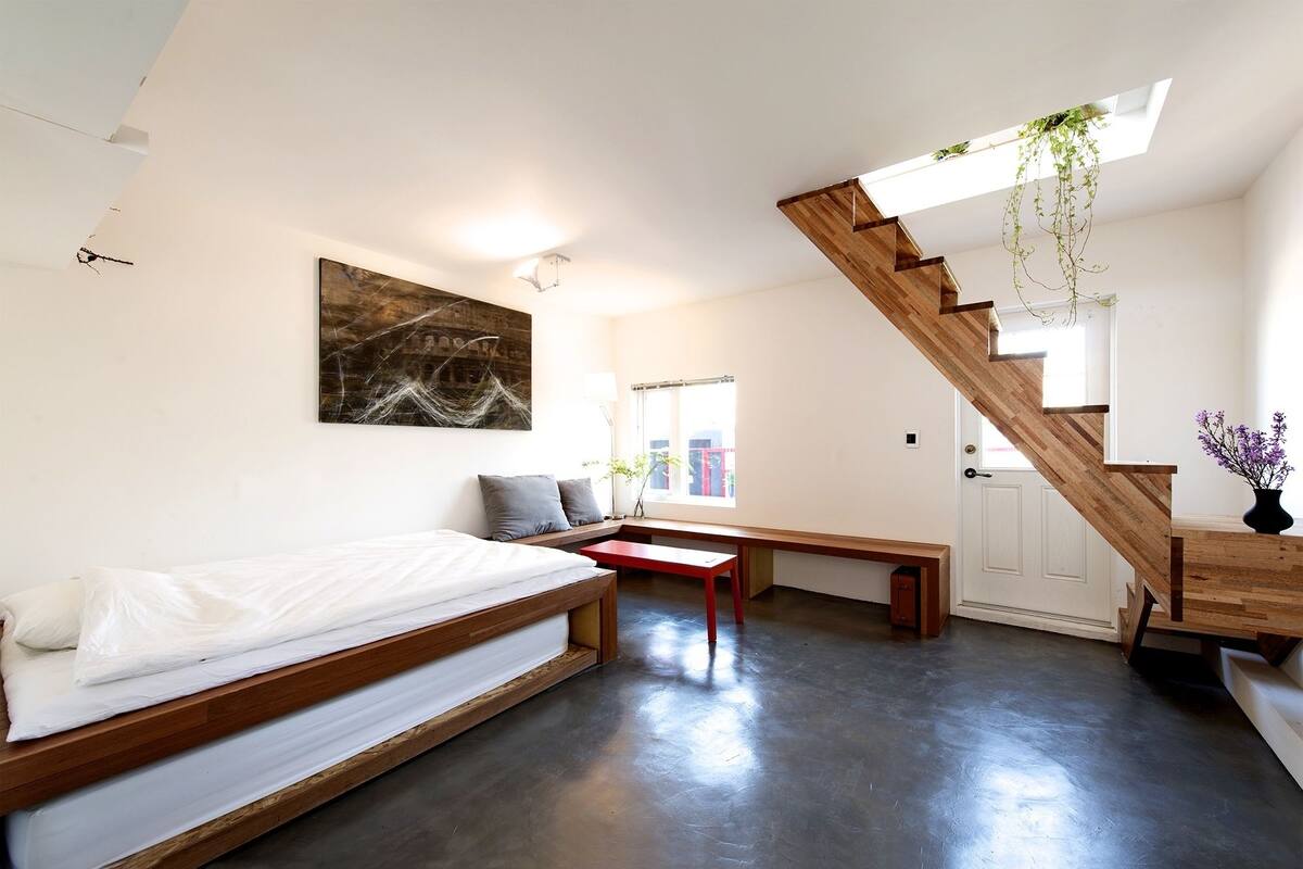 A modern bedroom with a loft bed, a wooden staircase, and a view of the outside.
