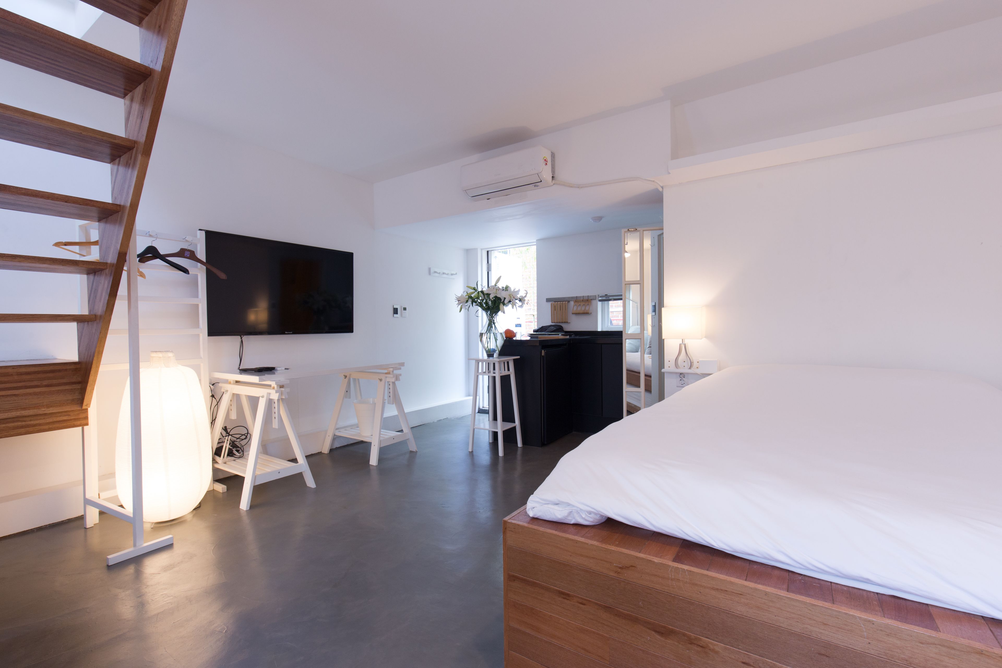 A modern bedroom with a wooden bed, a TV mounted on the wall, and a staircase.