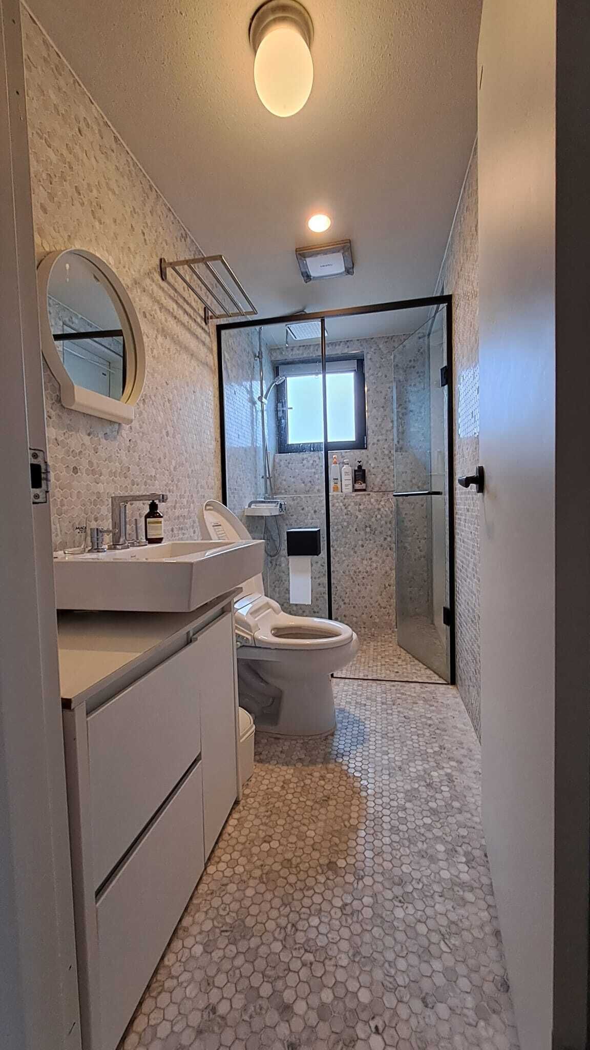 A bathroom with a toilet, sink, and shower area, featuring hexagonal tile flooring and a round mirror.