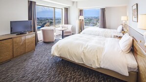 A hotel room with two beds, a TV, a desk, and a view of a cityscape.
