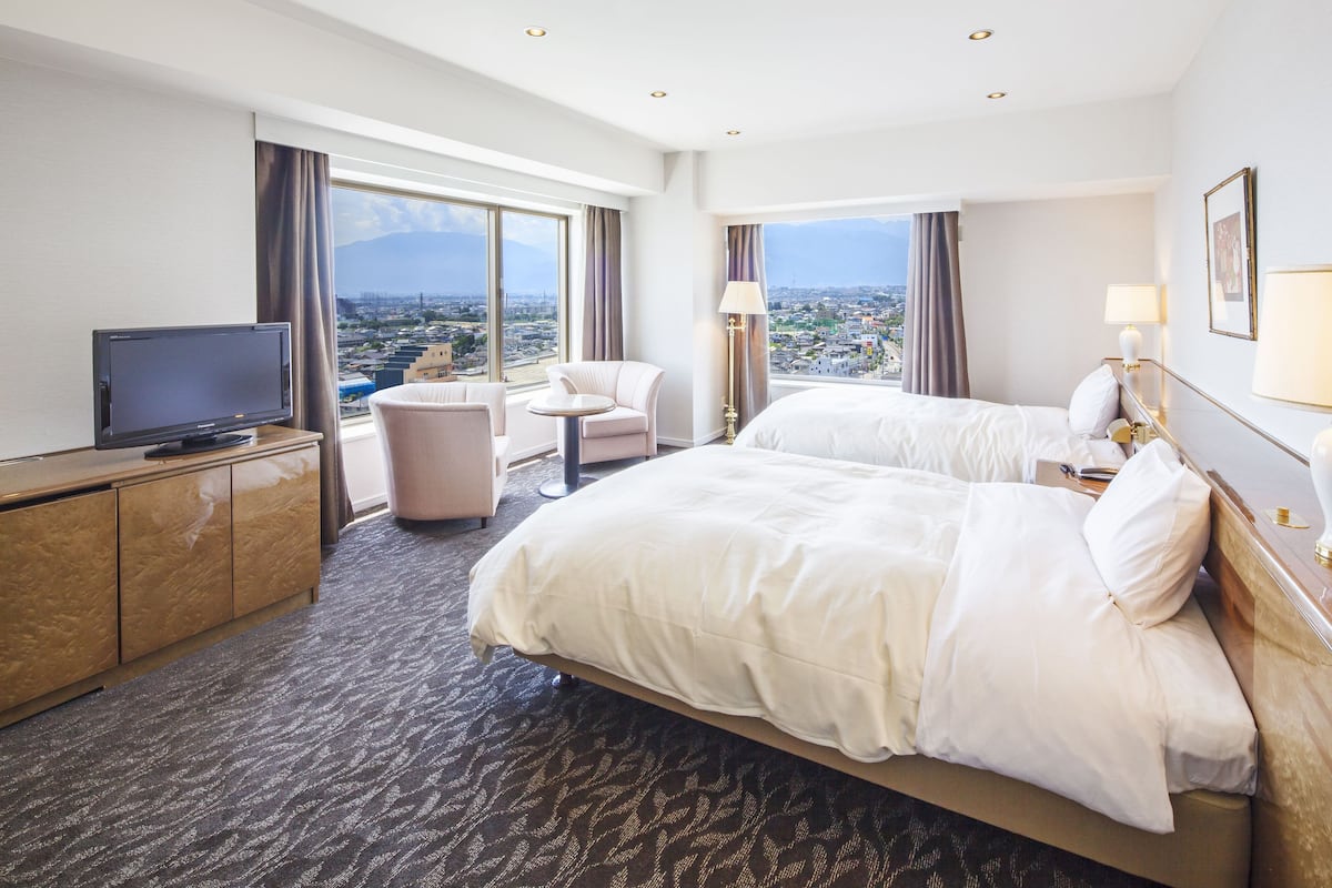 A hotel room with two beds, a TV, a desk, and a view of a cityscape.