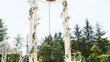 A white archway with a bell, surrounded by greenery and a clear sky.