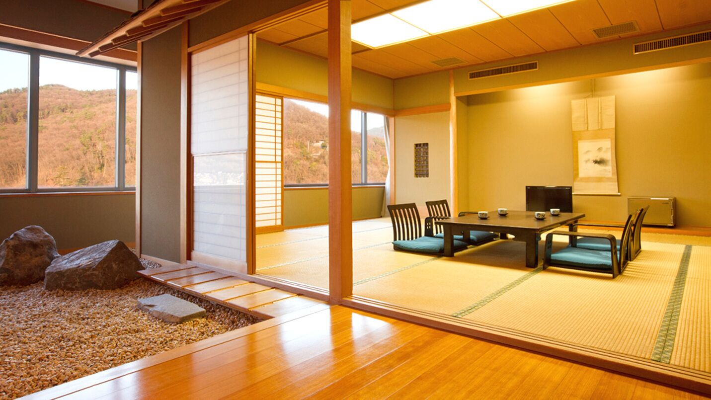 Une pièce de style japonais traditionnel, avec un sol recouvert de tatamis, une table basse avec des coussins et une vue sur une colline boisée.