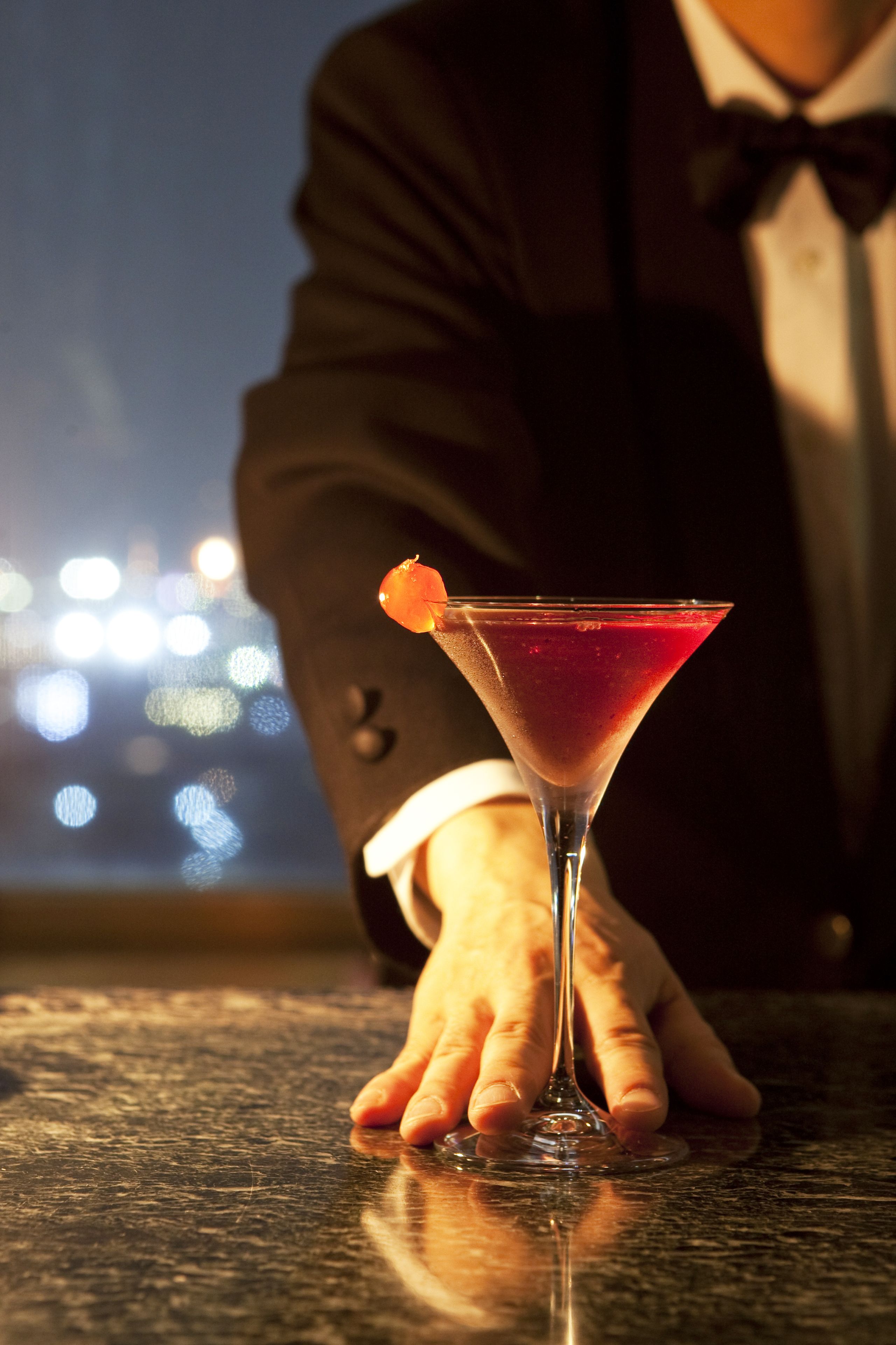 Una copa de martini con una bebida roja y una guarnición de naranja sobre una barra.