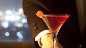 Una copa de martini con una bebida roja y una guarnición de naranja sobre una barra.