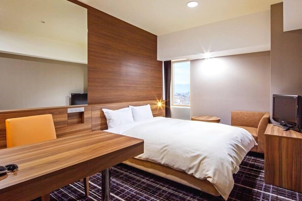 A hotel room with a bed, a desk, a chair, a television, and a window with a view.