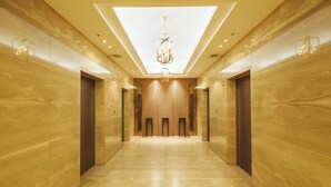 A modern hallway with a skylight, elevators, and a central chandelier.
