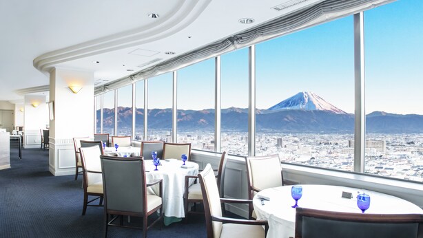 A restaurant with tables and chairs, large windows, and a view of a mountain.