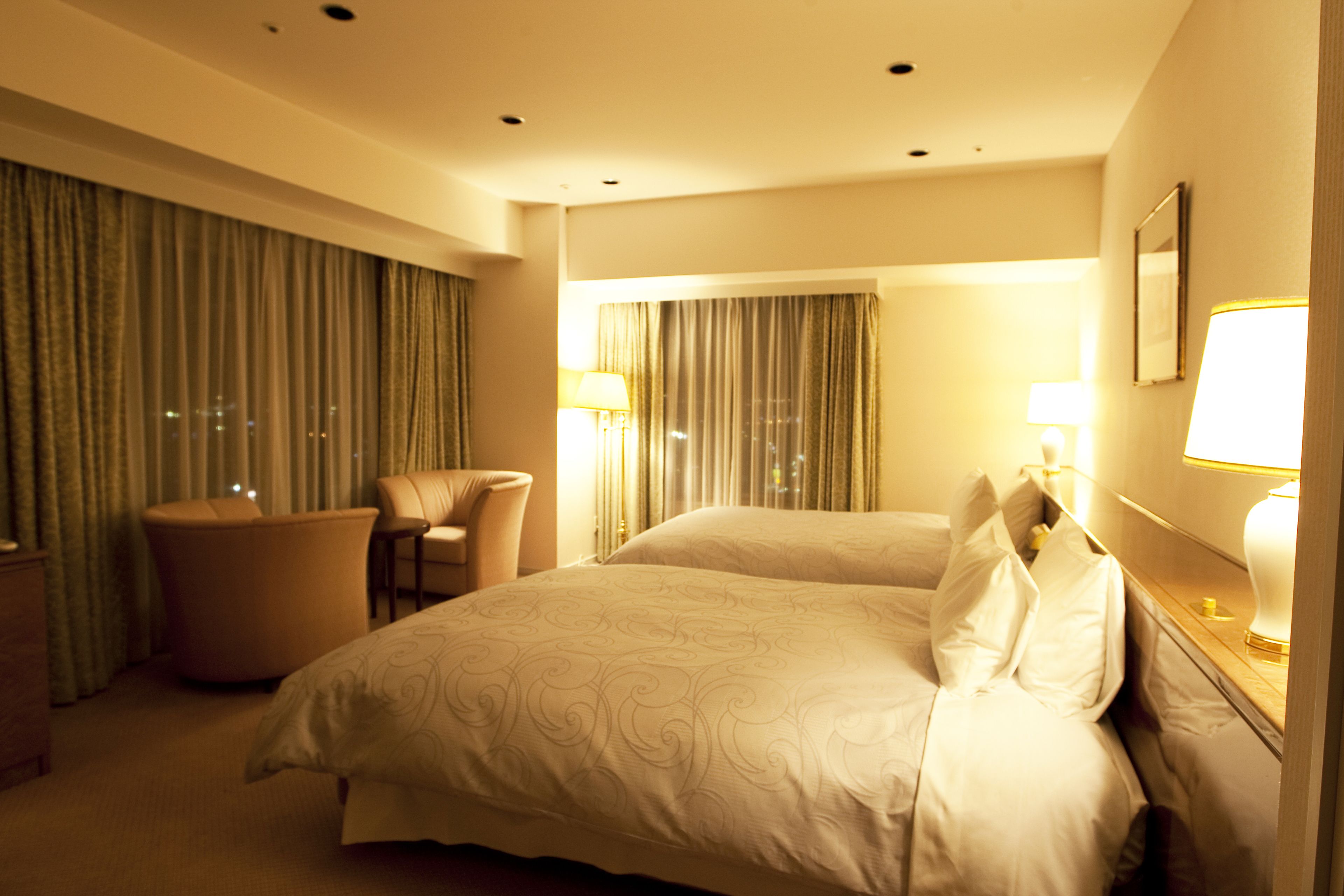 Una habitación de hotel con una cama grande, una silla, un escritorio con lámpara y cortinas en las ventanas.