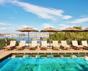 Una piscina al aire libre, sombrillas, sillones reclinables de piscina