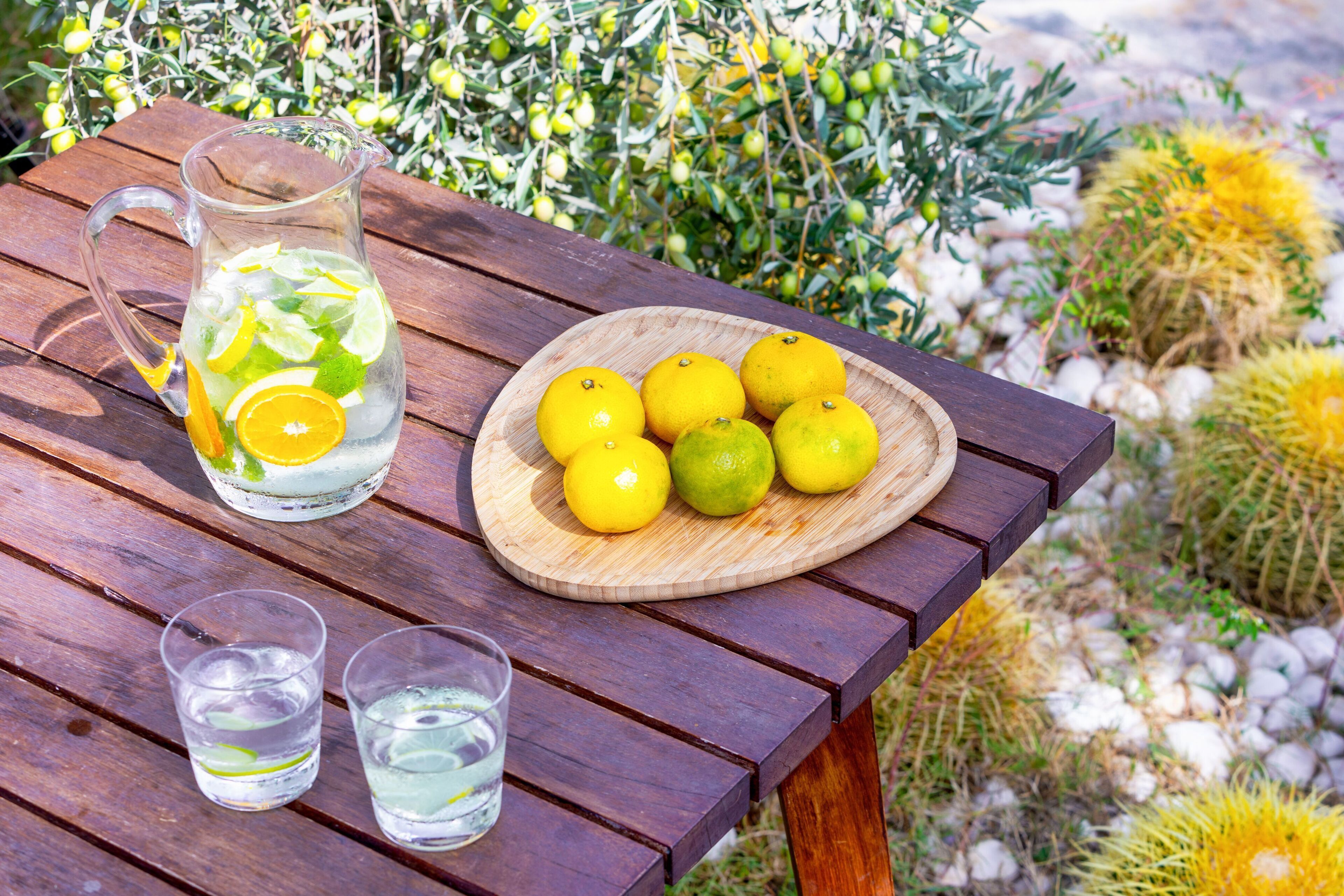 Een houten tafel met een limonadekan, een houten bord met citroenen en twee glaasjes water.