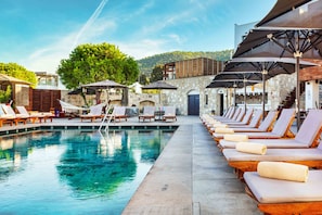Una piscina al aire libre, sombrillas, sillones reclinables de piscina