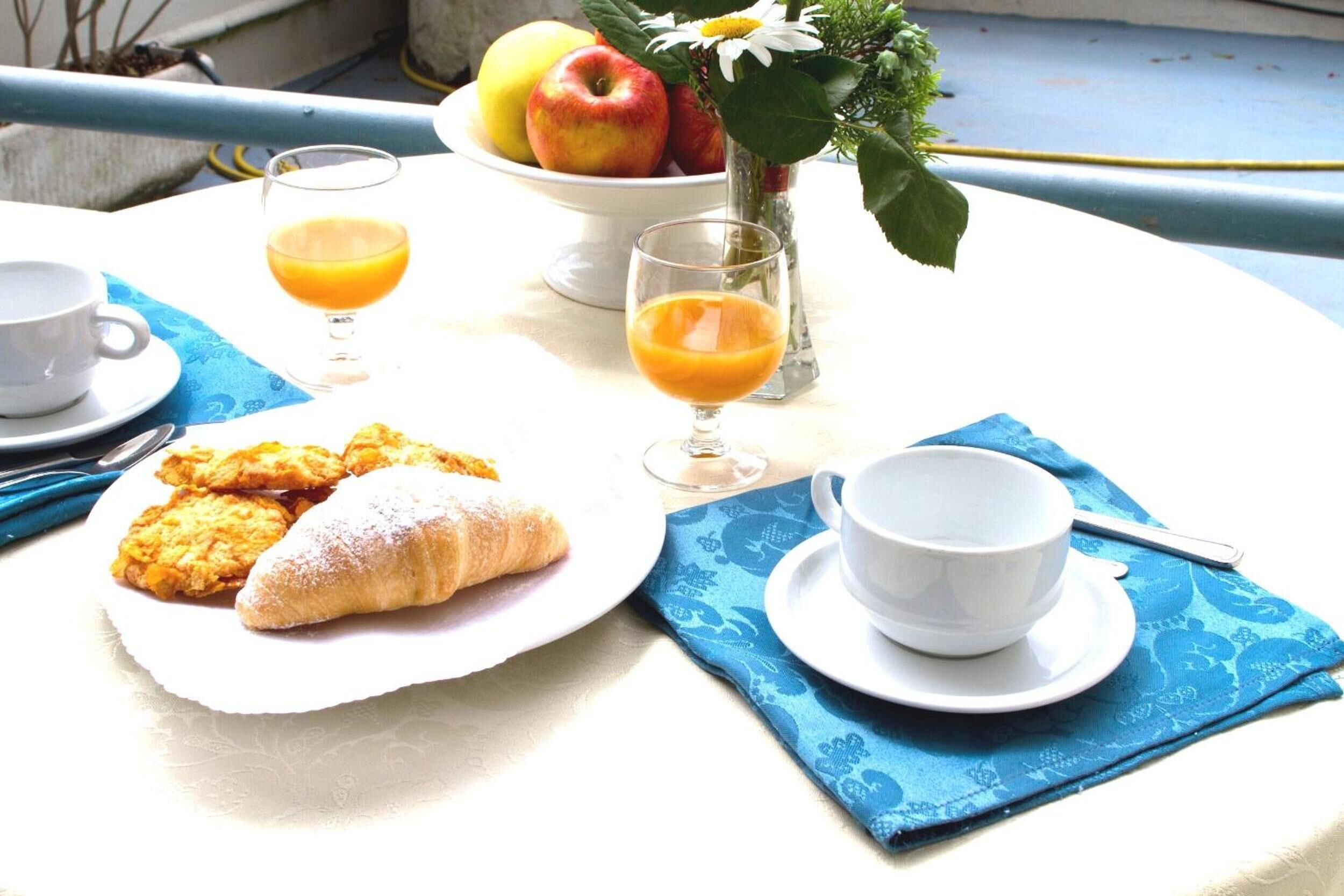 A breakfast setup with croissants, orange juice, and a bowl of fruit on a table.