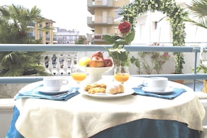 A table set with breakfast items, including fruits, pastries, and beverages, on a balcony with a railing and potted plants. - Hotel Vienna (Bellaria-Igea Marina)