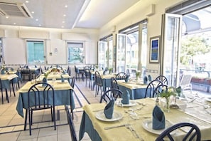 A restaurant with multiple tables set for dining, large windows, and a view of the outdoors. - Hotel Vienna (Bellaria-Igea Marina)
