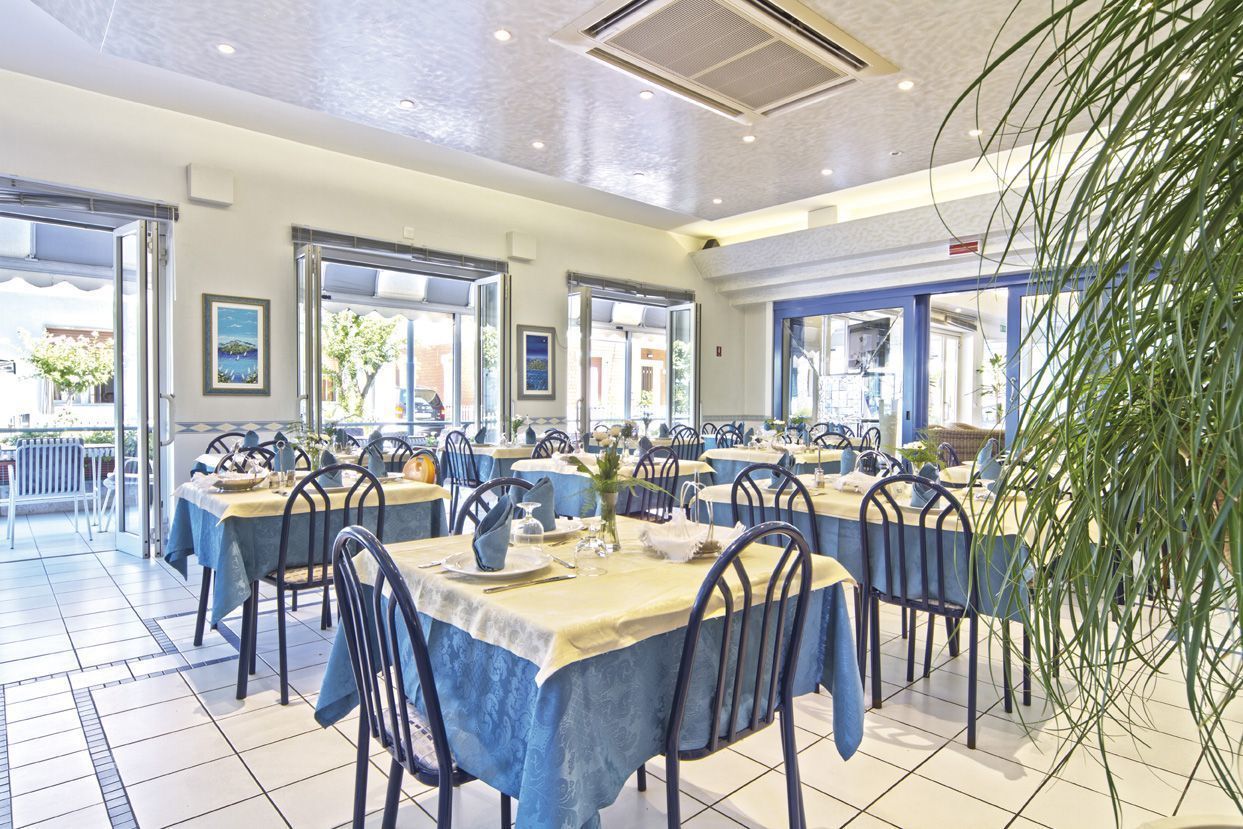 A spacious dining area with multiple tables set for guests, featuring blue tablecloths and metal chairs.
