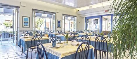 A spacious dining area with multiple tables set for guests, featuring blue tablecloths and metal chairs.