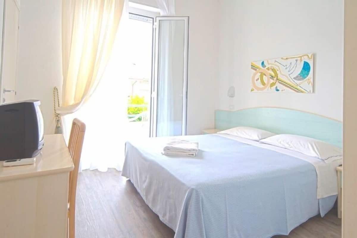Une chambre d’hôtel avec un lit, un bureau, une télévision et une fenêtre avec des rideaux.