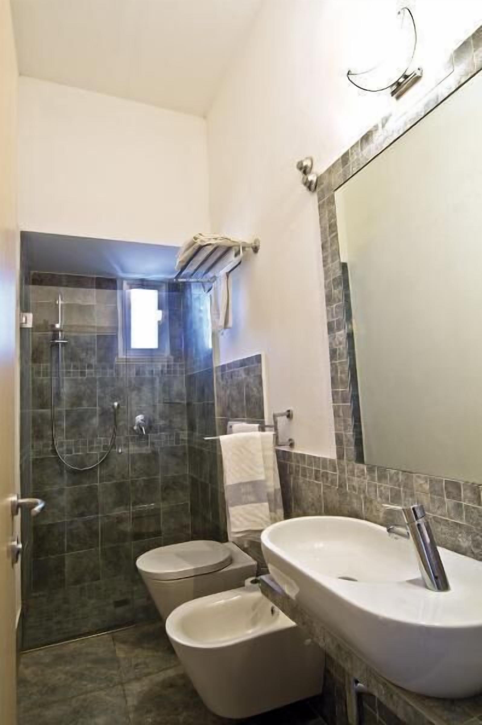 A bathroom with a glass-enclosed shower, a white sink, and two toilets.