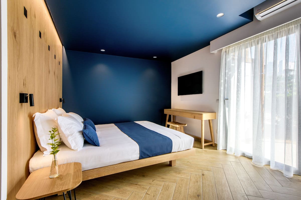 A modern bedroom with a wooden bed, a small desk, and a large window with sheer curtains.
