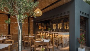 Un área de comedor al aire libre con mesas y sillas de madera, un muro de piedra con cuadros enmarcados y una lámpara colgante.