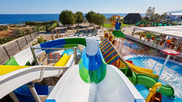 Un parque acuático con múltiples toboganes y una zona de piscina, rodeado de árboles y vistas al mar.