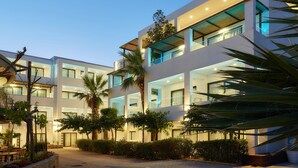 Un hotel moderno de varios pisos con balcones, mobiliario exterior y jardines exuberantes.