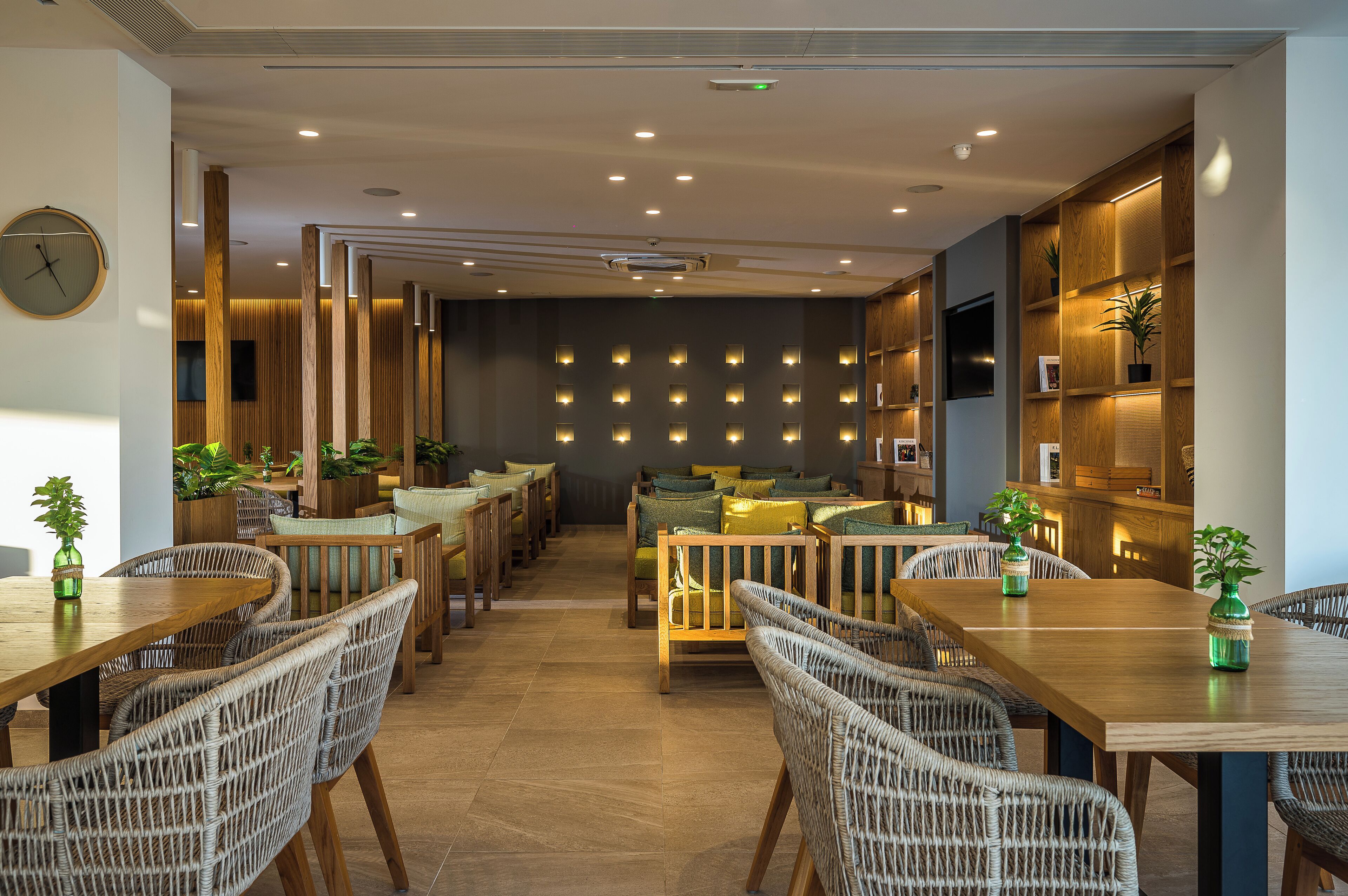 A modern dining area with wicker chairs, wooden tables, and a wall of illuminated square lights.