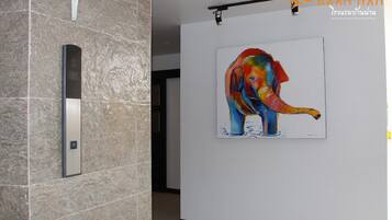 Un pasillo con pared de azulejos, un cuadro de un elefante colorido y un letrero con texto tailandés.