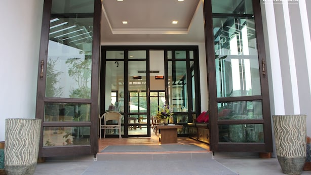 Entrada de hotel con puerta de cristal, un mostrador de recepción y una zona de estar con sillas y una mesa.