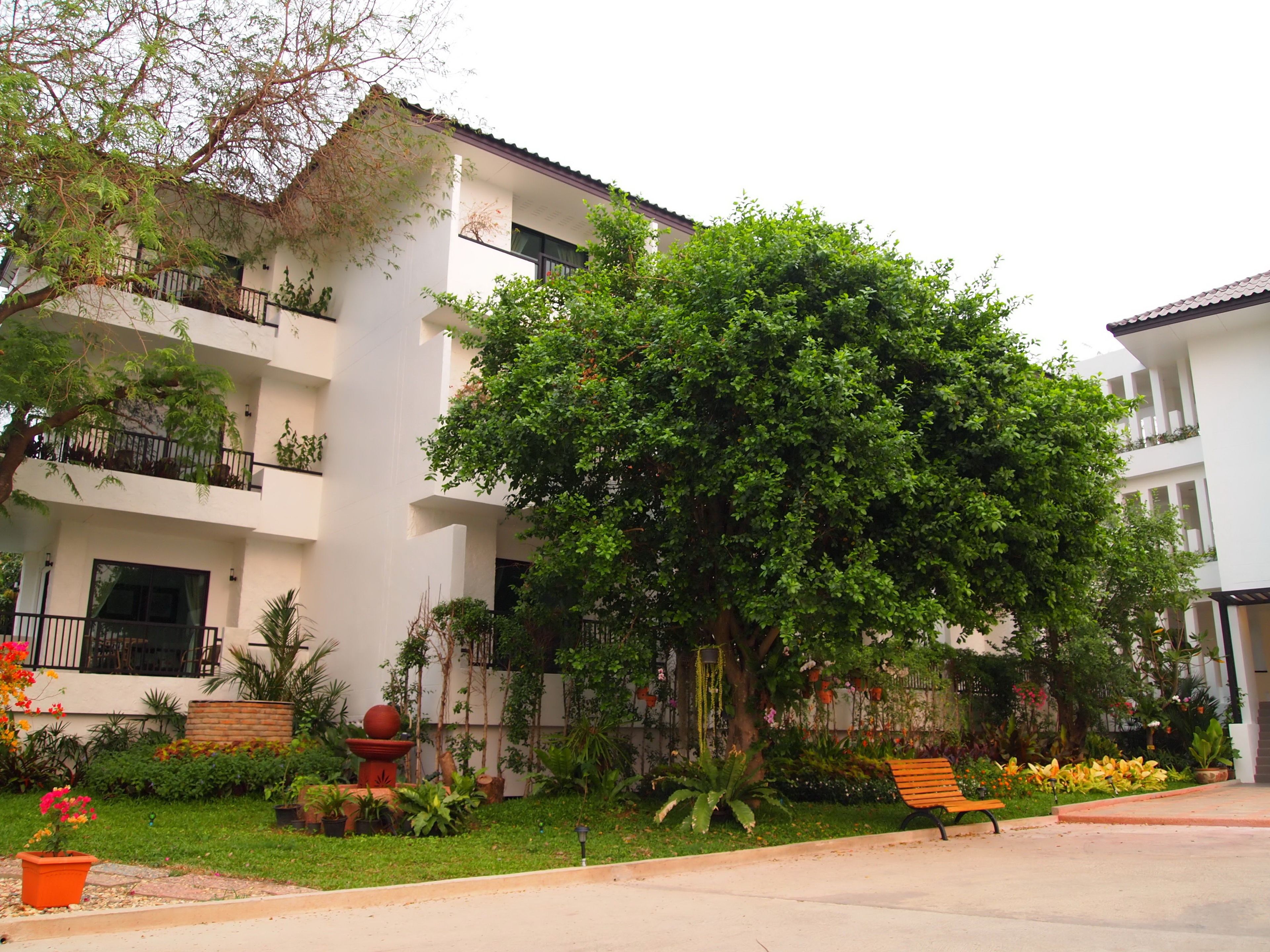 A multi-story building with balconies, surrounded by lush greenery and a well-maintained garden.